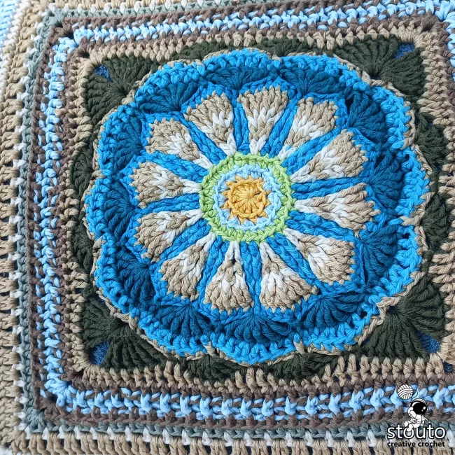 Close-up of a textured heirloom flower granny square showing detailed crochet stitches and floral petals.